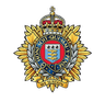 The cap badge of the Royal Logistic Corps: a crowned garter inscribed 'Honi Soit Qui Mal Y Pense' surrounding the corps shield, flanked by laurel and a gold sunburst, with the motto 'We Sustain' beneath.